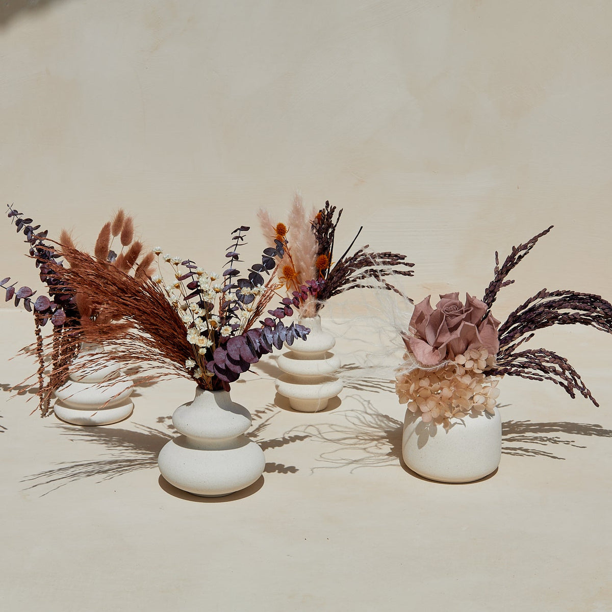 Stoneware bud vases holding dried floral arrangements in earthy tones for table decor