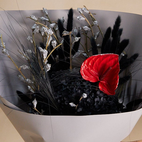 A black preserved floral arrangement with a red anthurium flower