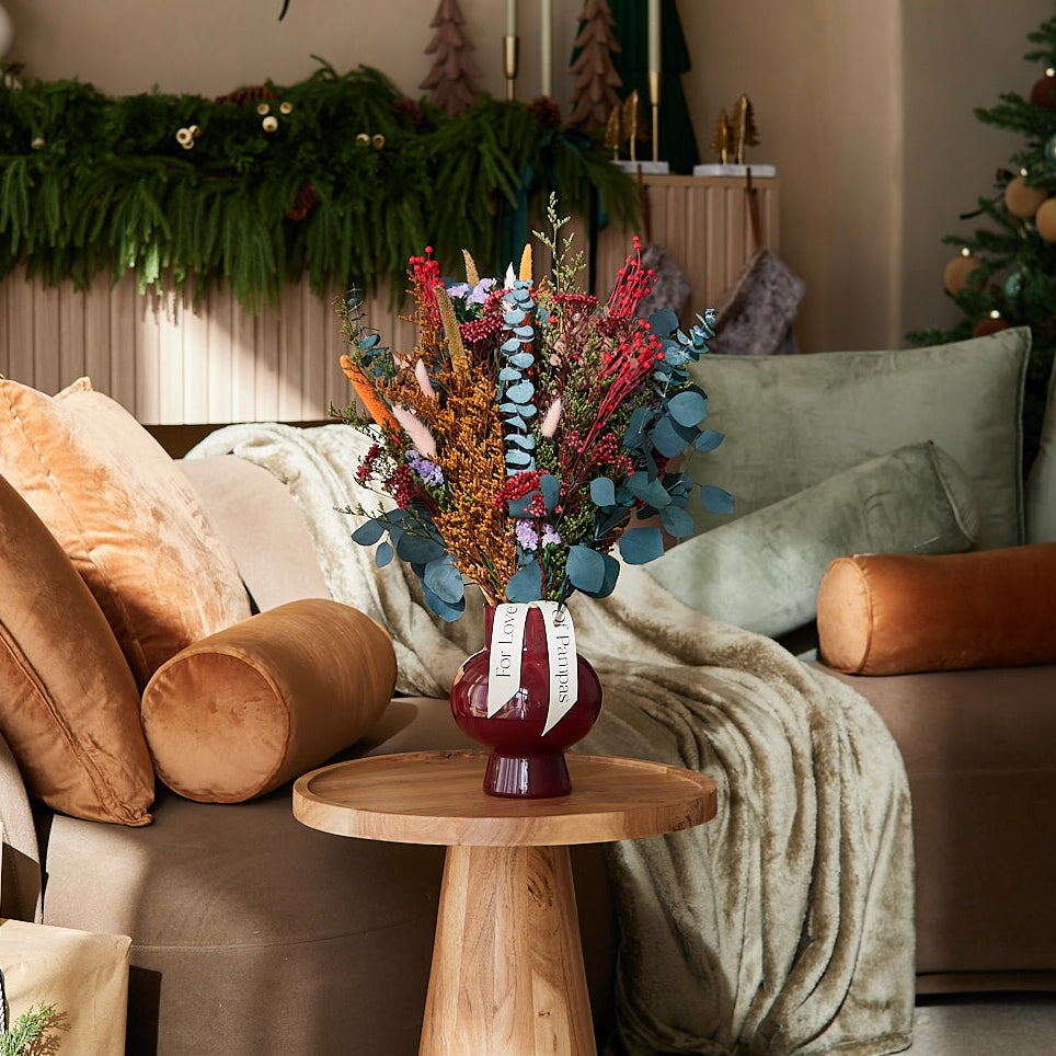 


Preserved flower bouquet in a vase on a small wooden table in a Christmas decorated living room.
