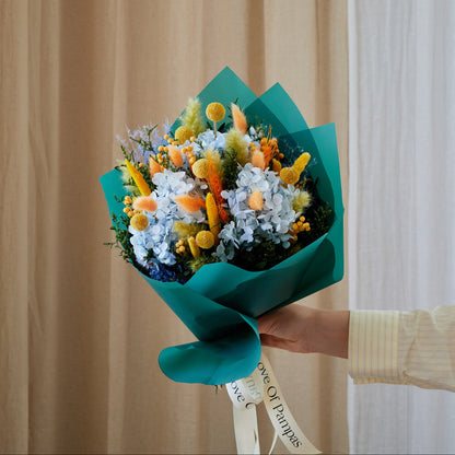 Bouquet of preserved flowers wrapped in teal paper held by a person against a neutral background